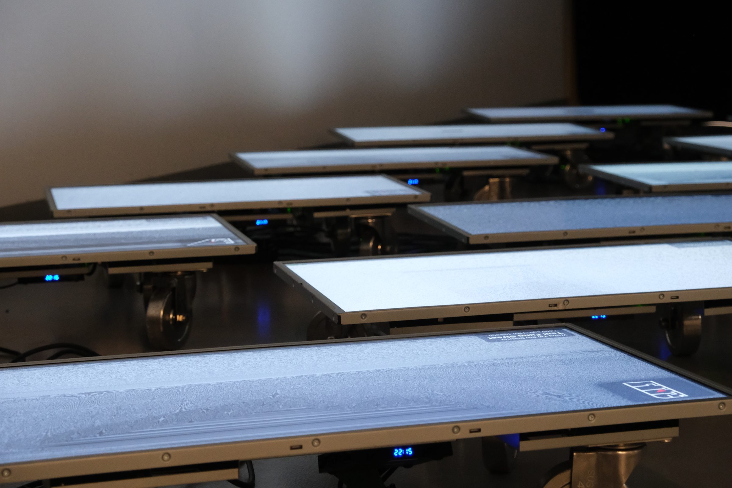 Rows of flatbed trolleys, each carrying a screen showing grey reconstructed interiors.